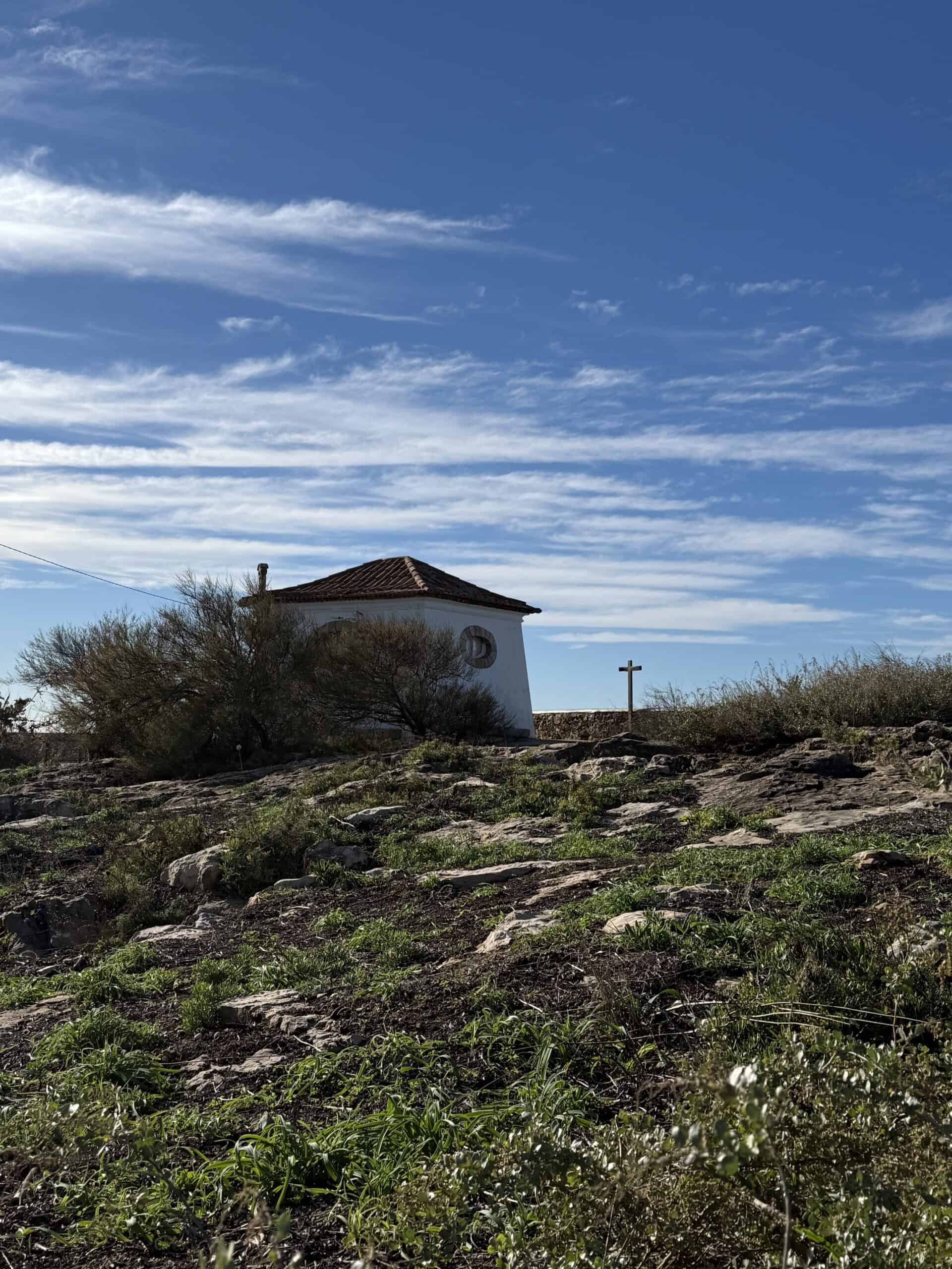 Small white building and stone cross among rocks and shrubs near Boca do Inferno in Cascais.