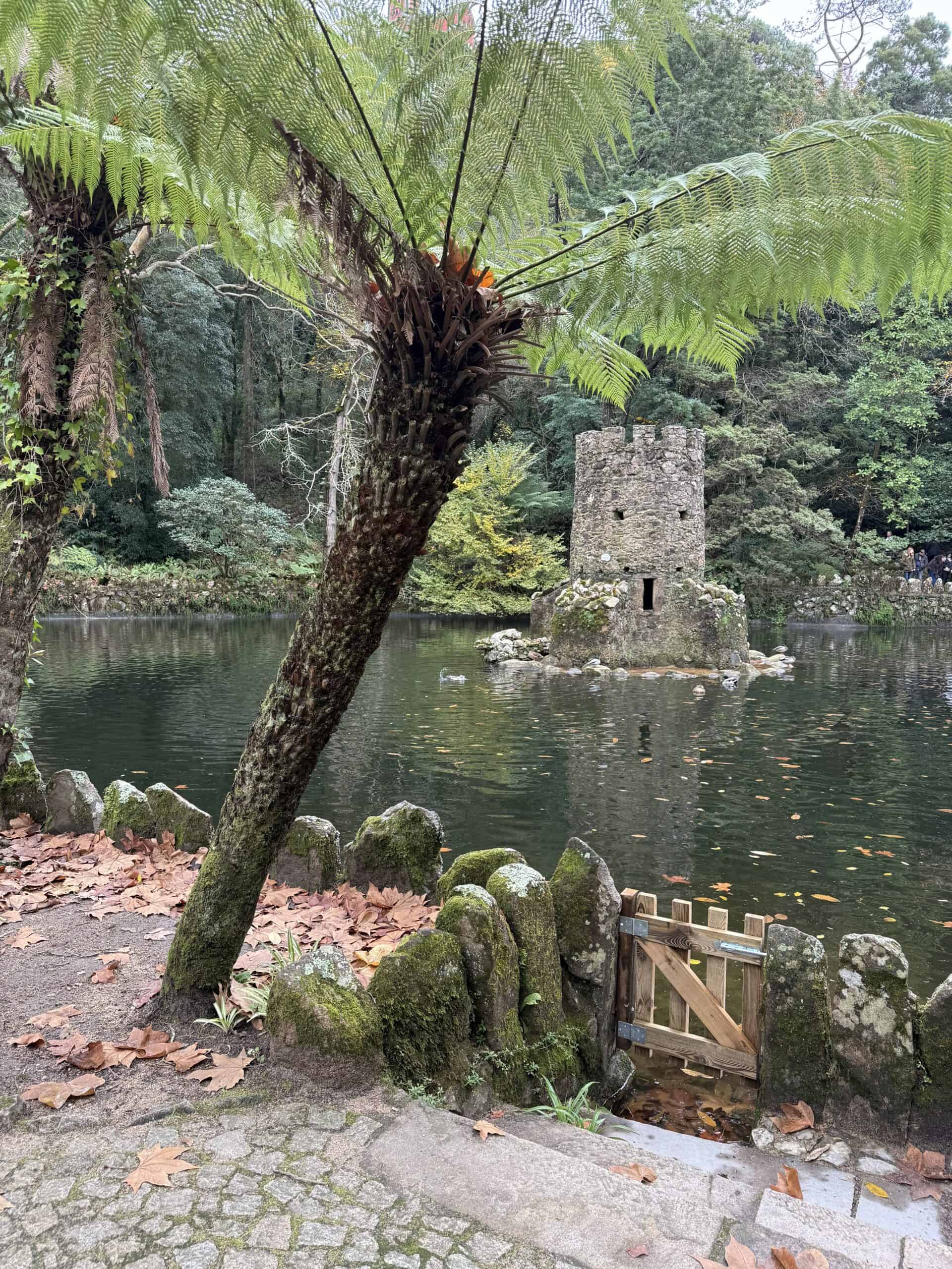 Caminho dos Lagos in Pena Park with a stone tower in the lake surrounded by lush greenery in Sintra.