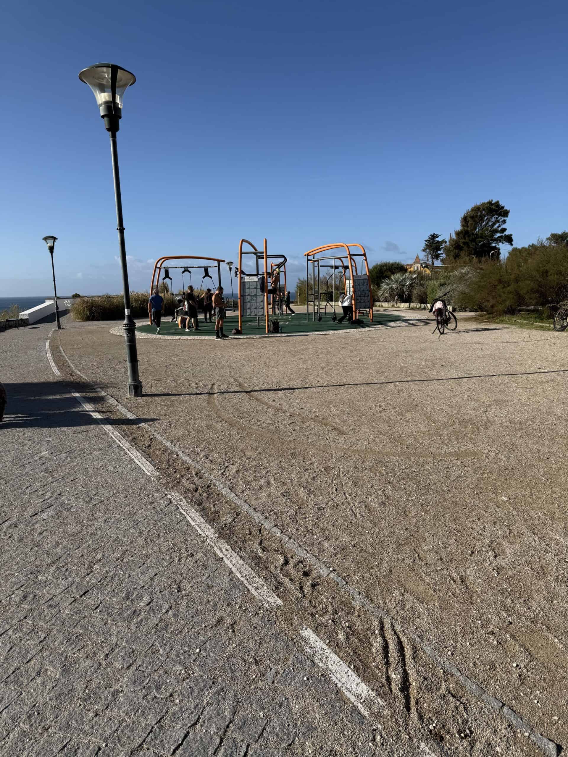 Outdoor fitness park with orange exercise equipment and people training beside the Atlantic Ocean in Cascais, Portugal.