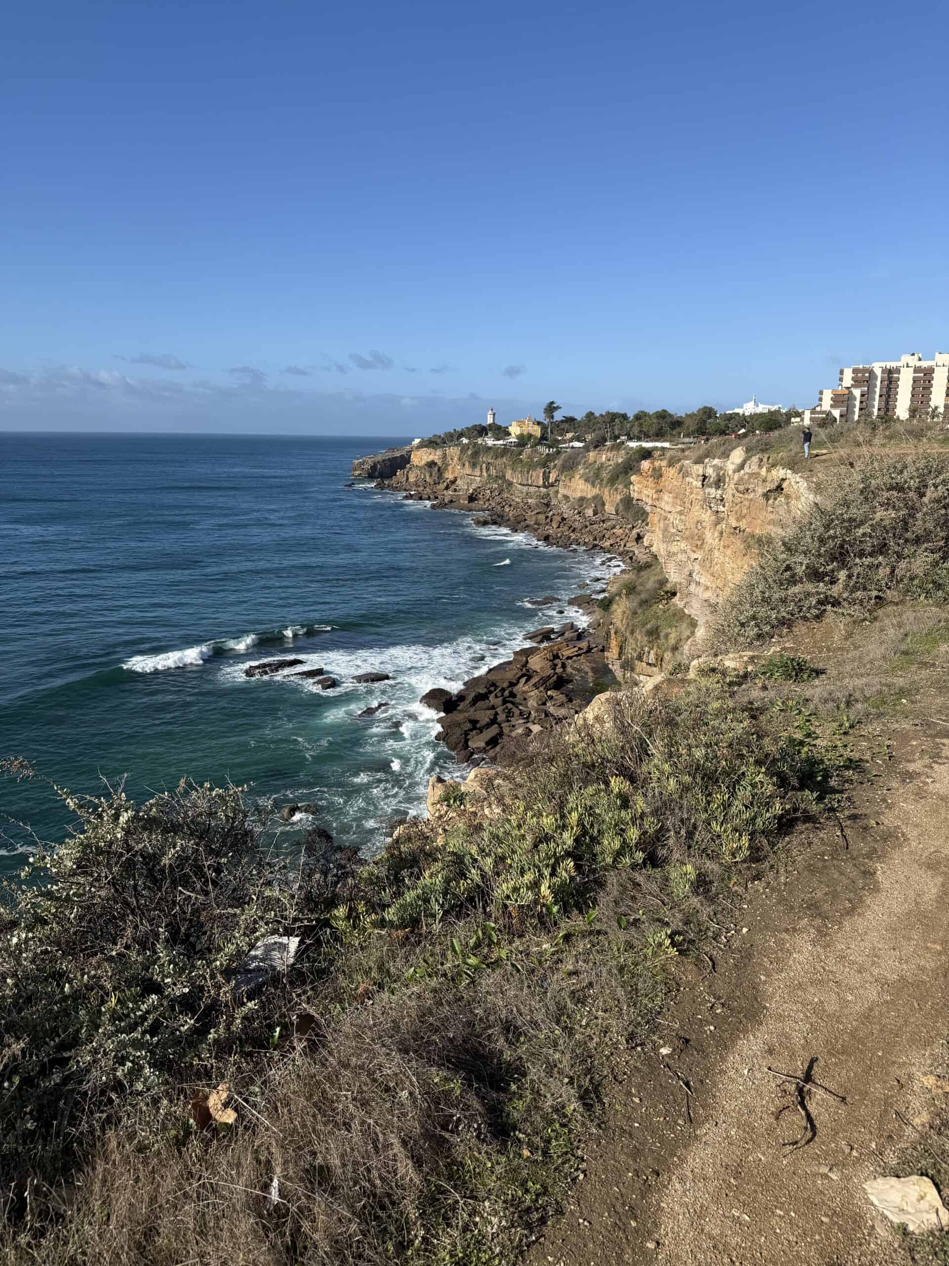 Rugged golden cliffs and rocky shoreline along the Cascais coast towards Guia, with Atlantic waves breaking below.