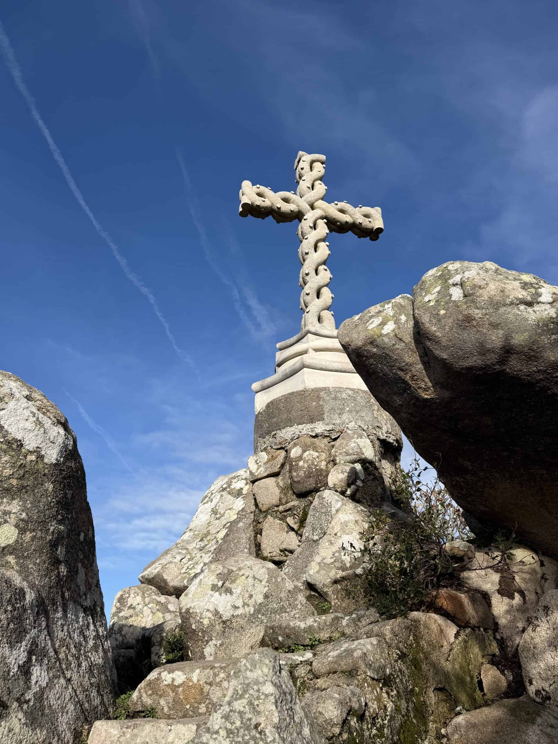 Stone cross at Cruz Alta in Pena Park, set among granite boulders beneath a bright blue sky.