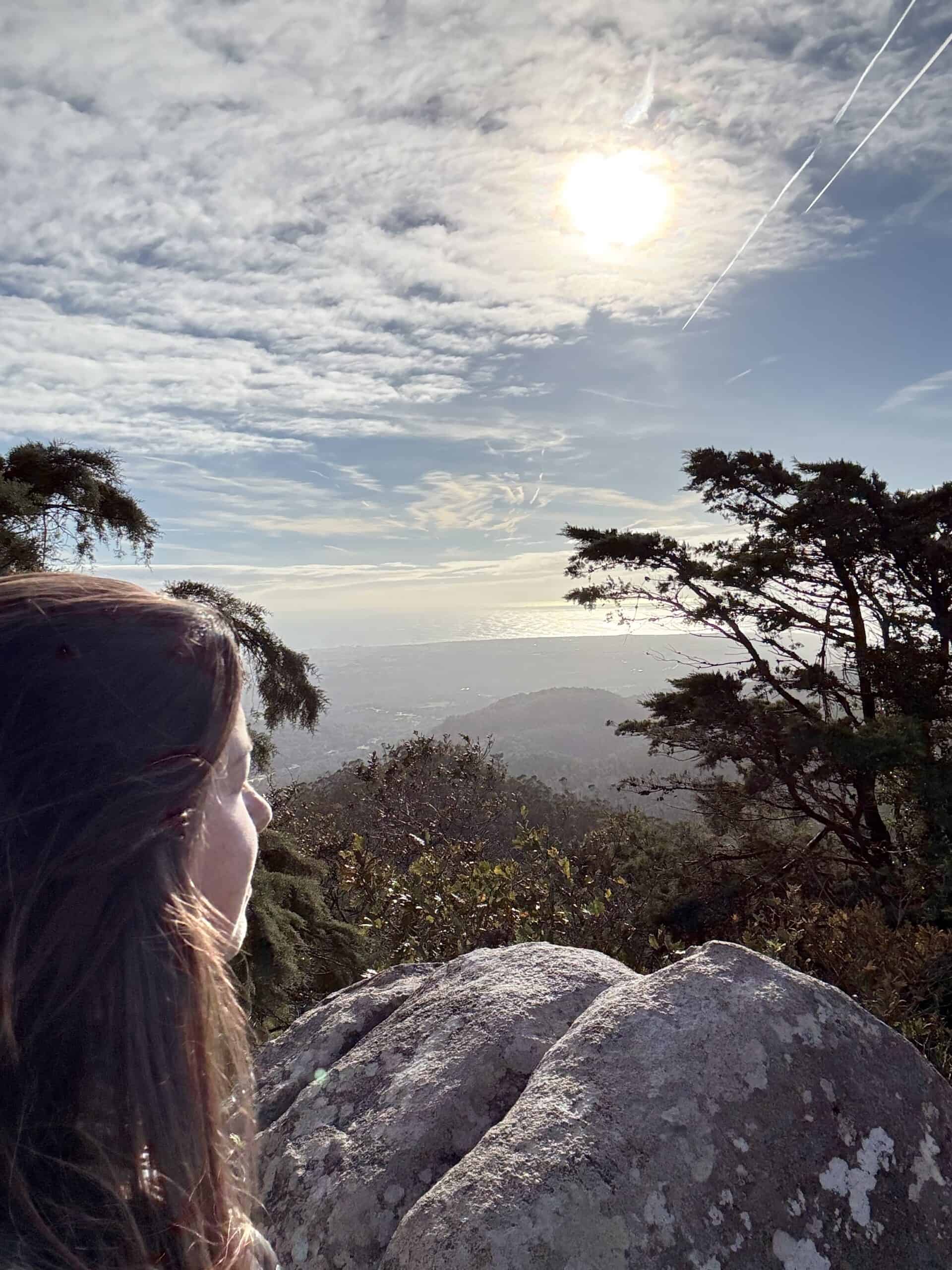 View from Cruz Alta over the Sintra hills toward the coast, with granite boulders and trees in the foreground.