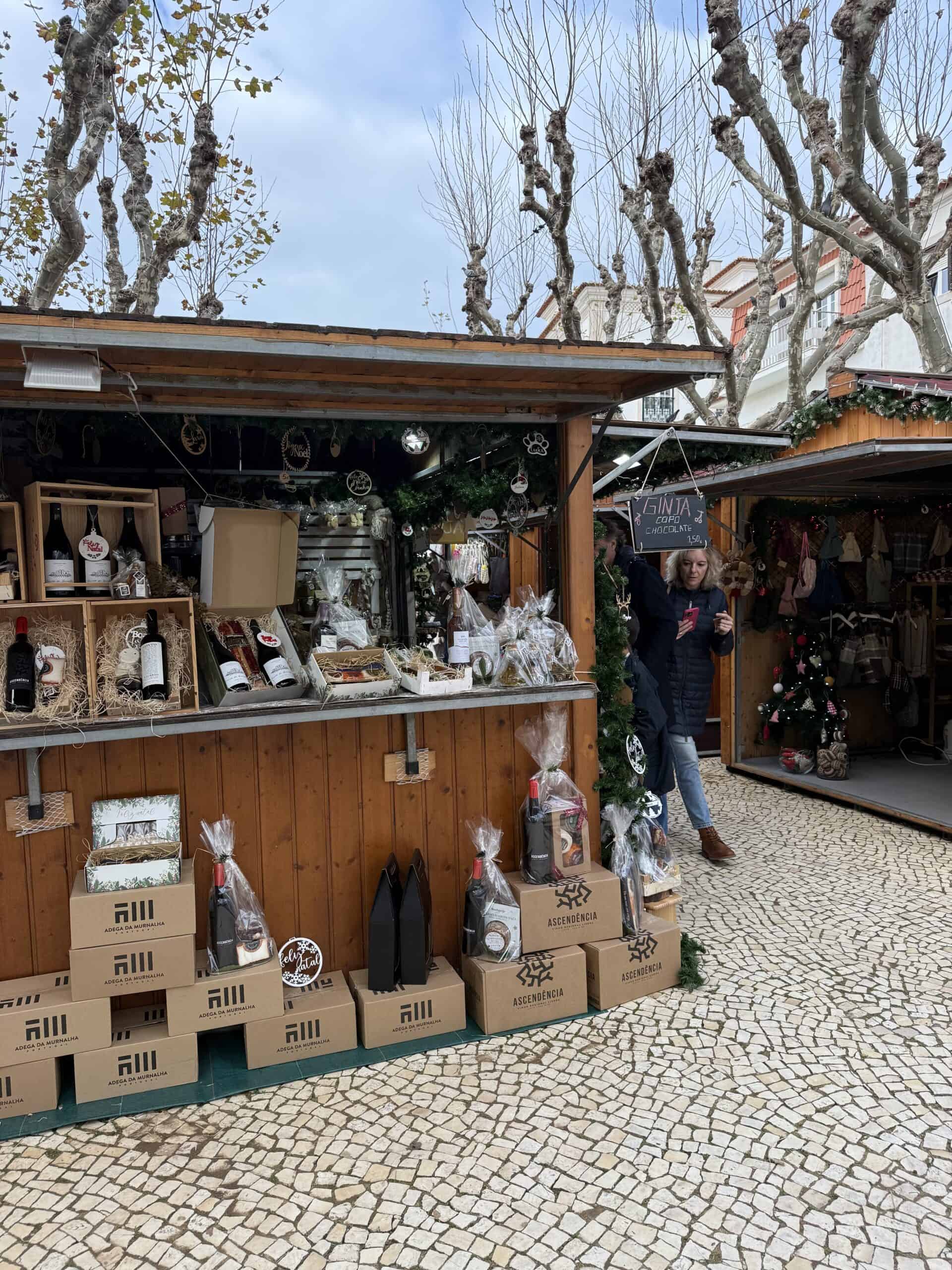 Wooden Christmas market stalls selling Portuguese wines, gift baskets, and festive decorations in Ericeira, Portugal.