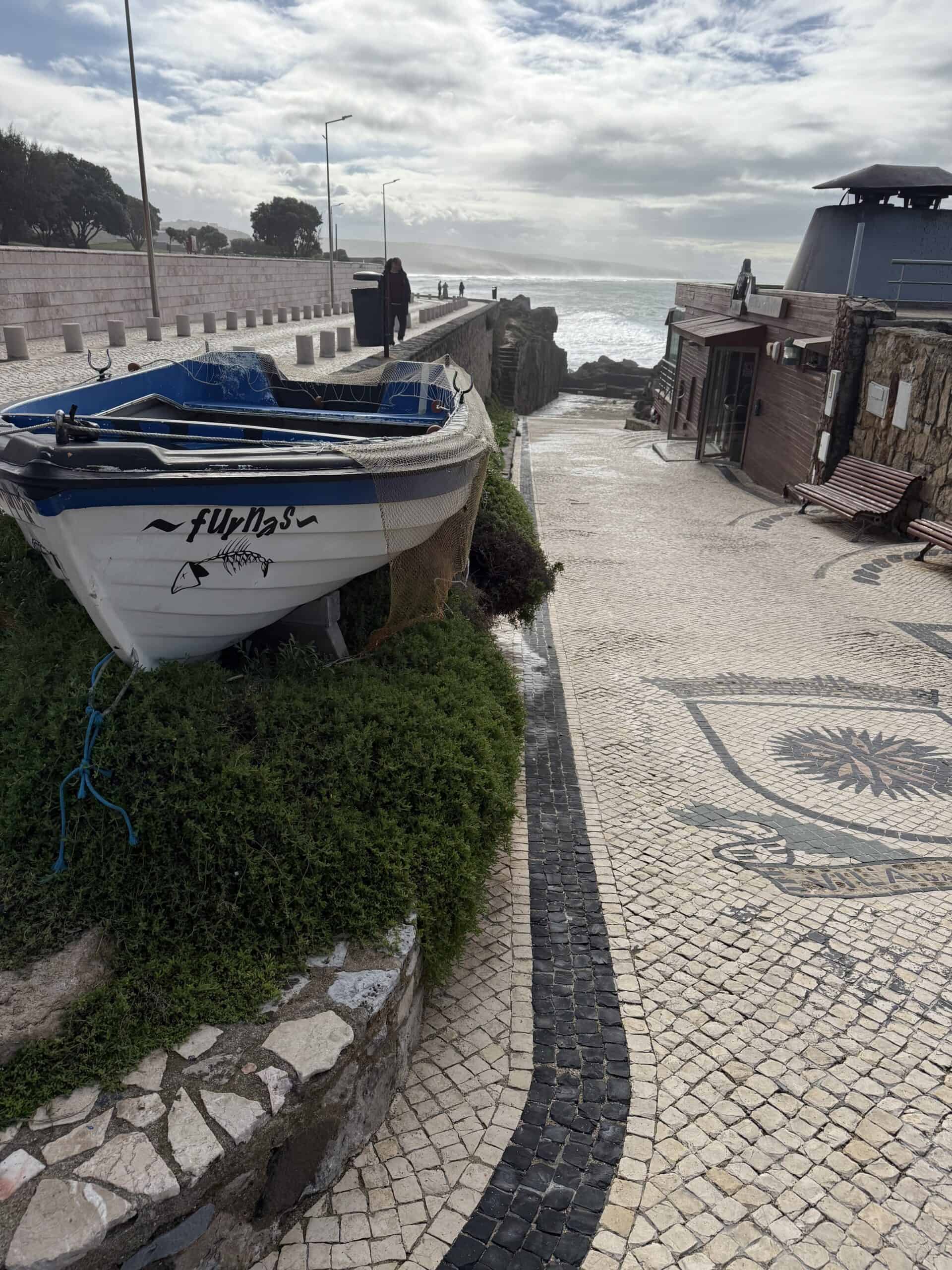Traditional fishing boat beside a cobblestone coastal promenade in Ericeira, Portugal.