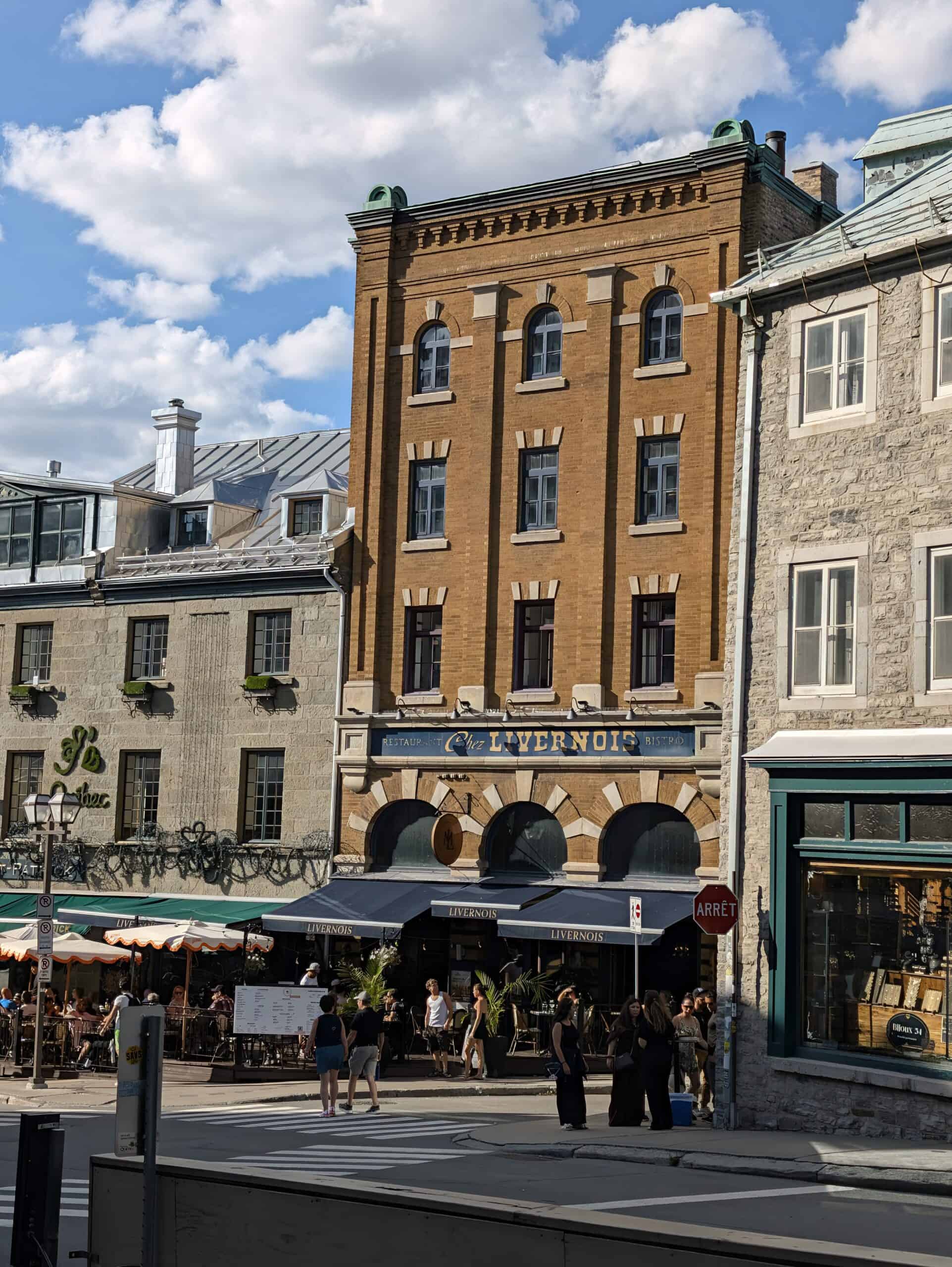 Historic brick facade of Le Livernois restaurant in Old Quebec City, with its outdoor terrace and guests enjoying a sunny afternoon.