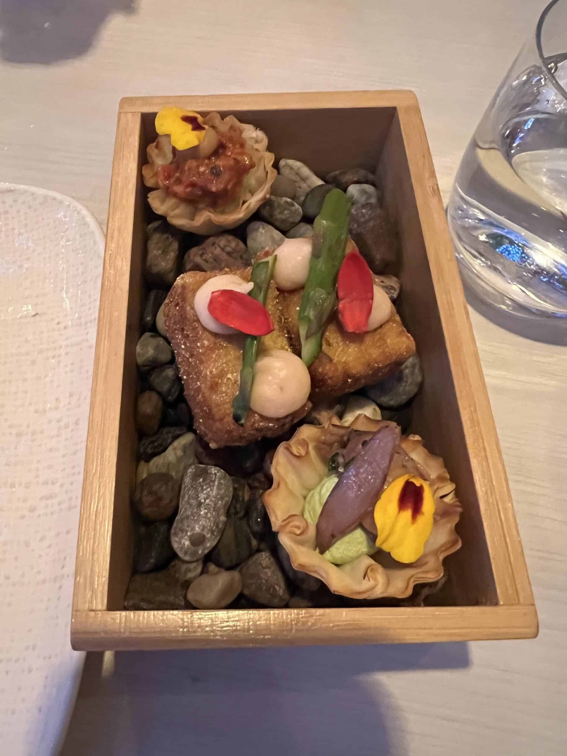 Creative appetizers from L'Orygine's discovery menu in Quebec City, served in a wooden box with stones and edible flowers.