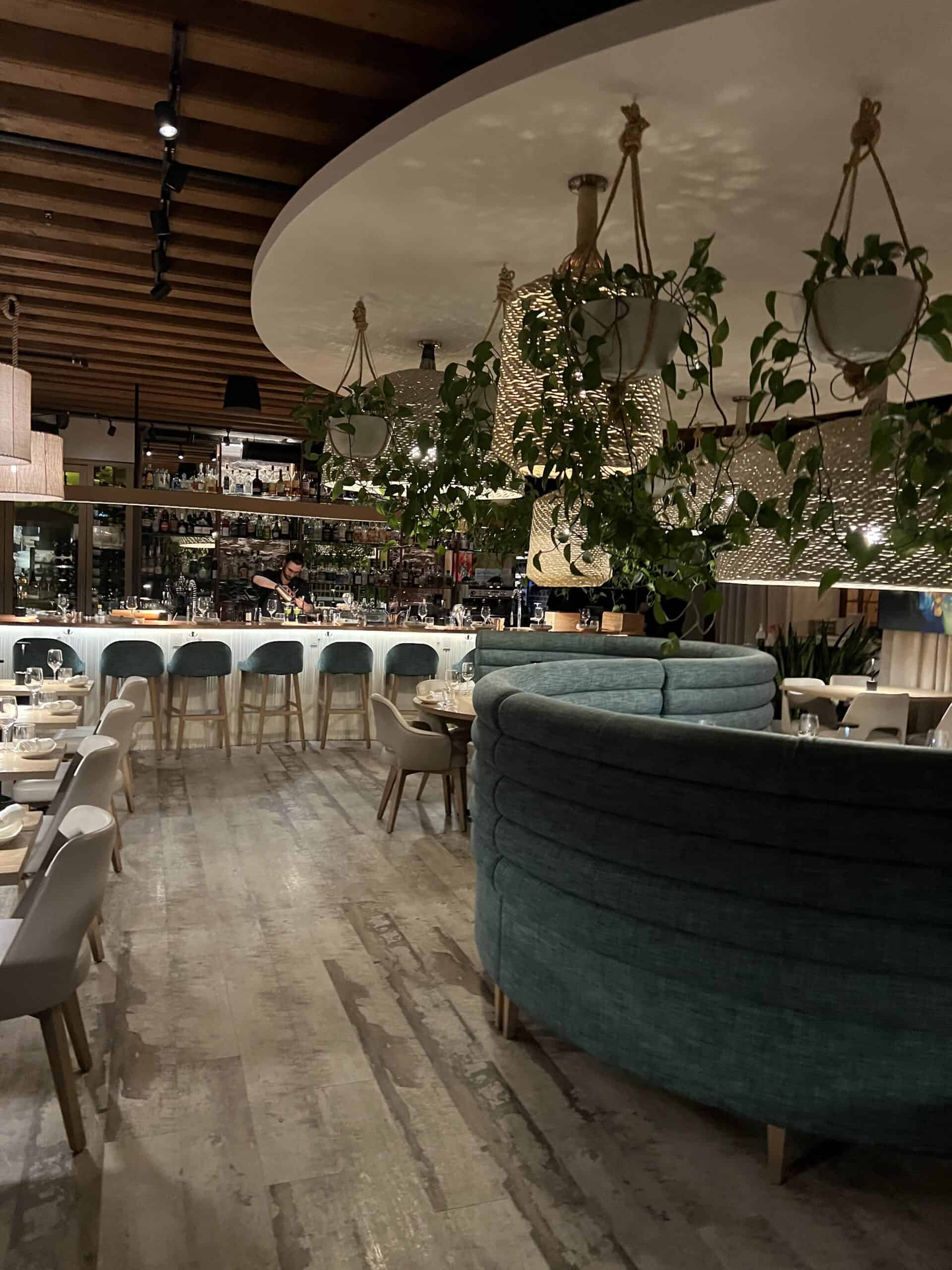 Elegant interior of L'Orygine restaurant in Old Quebec City, featuring hanging greenery, modern lighting and curved green seating.
