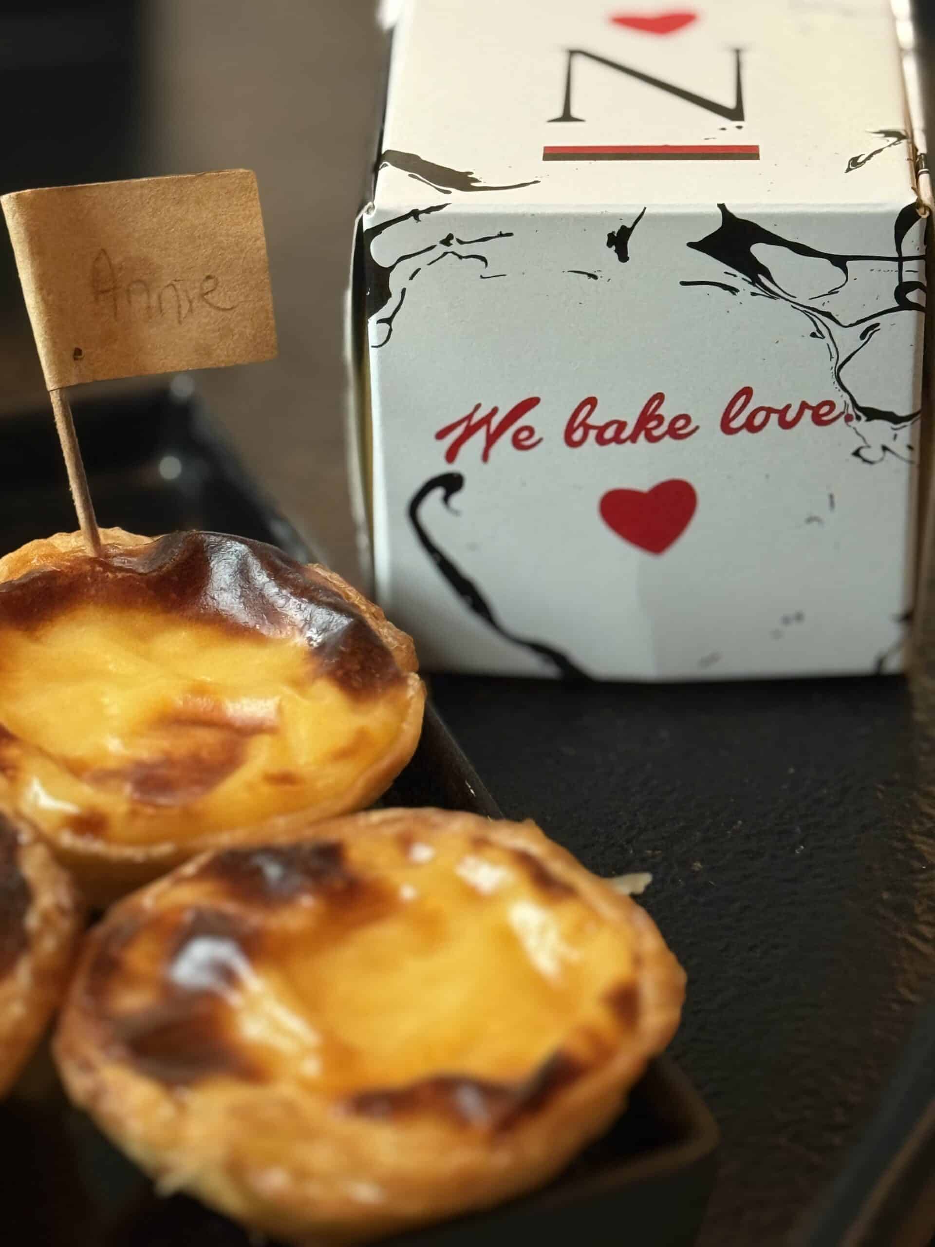 Freshly baked pastéis de nata from the Nat'elier masterclass in Lisbon, with a personalized flag and takeaway box.