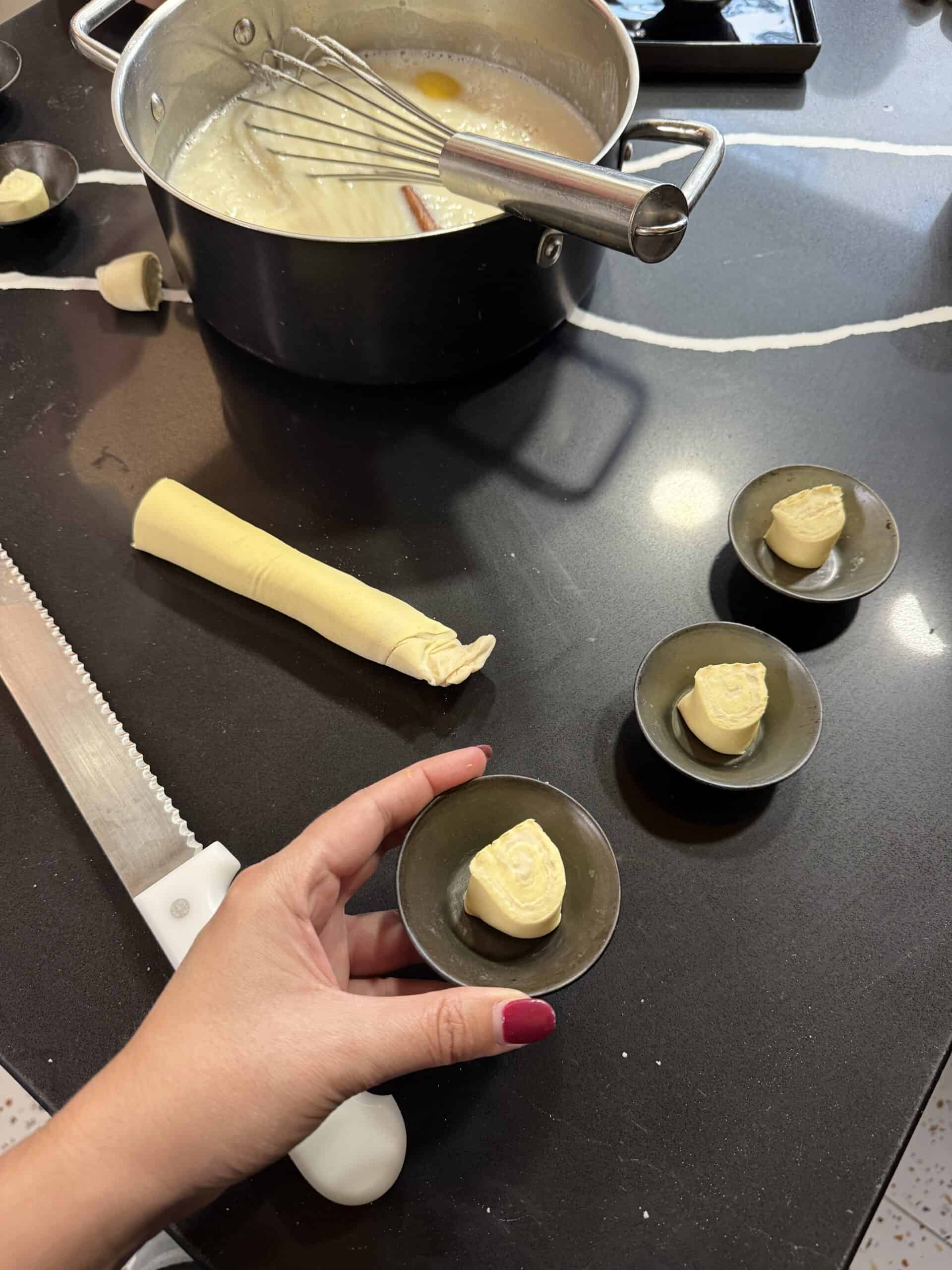 Preparing pastel de nata pastry at the Nat'elier cooking class in Lisbon, with rolled dough, custard mixture and pastry moulds.