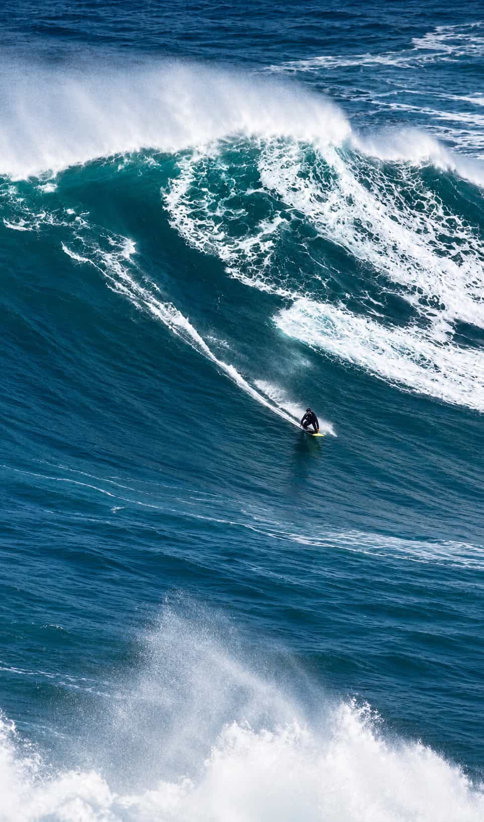 Professional big-wave surfer riding a giant wave at Praia do Norte in Nazaré, Portugal