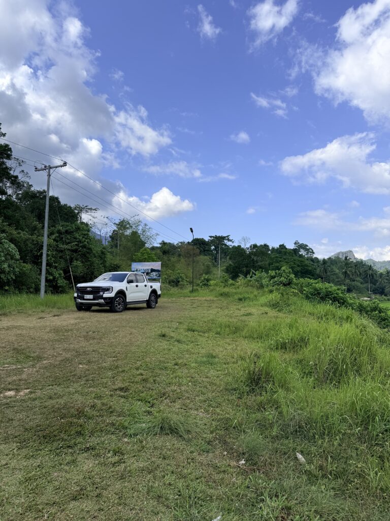 White Ford Ranger parked in a grassy clearing surrounded by tropical vegetation and distant hills in Palawan.