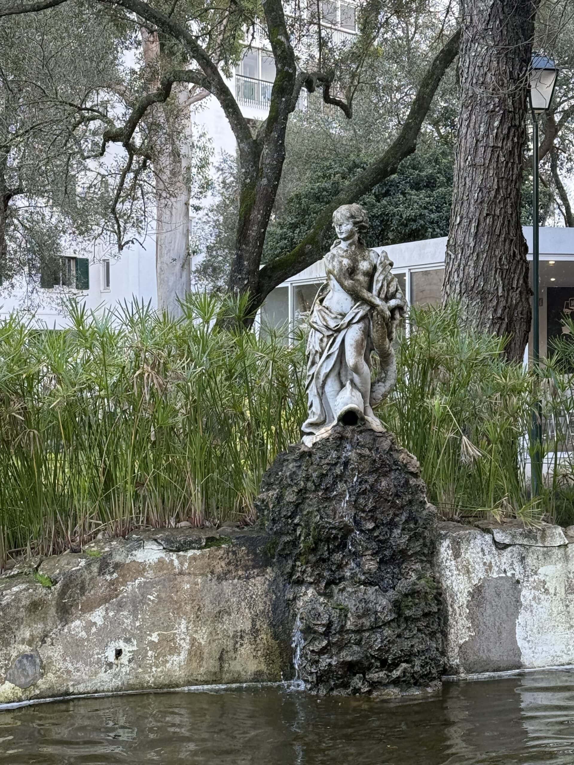Classical stone statue fountain surrounded by trees and greenery in Parque Marechal Carmona, Cascais, Portugal.