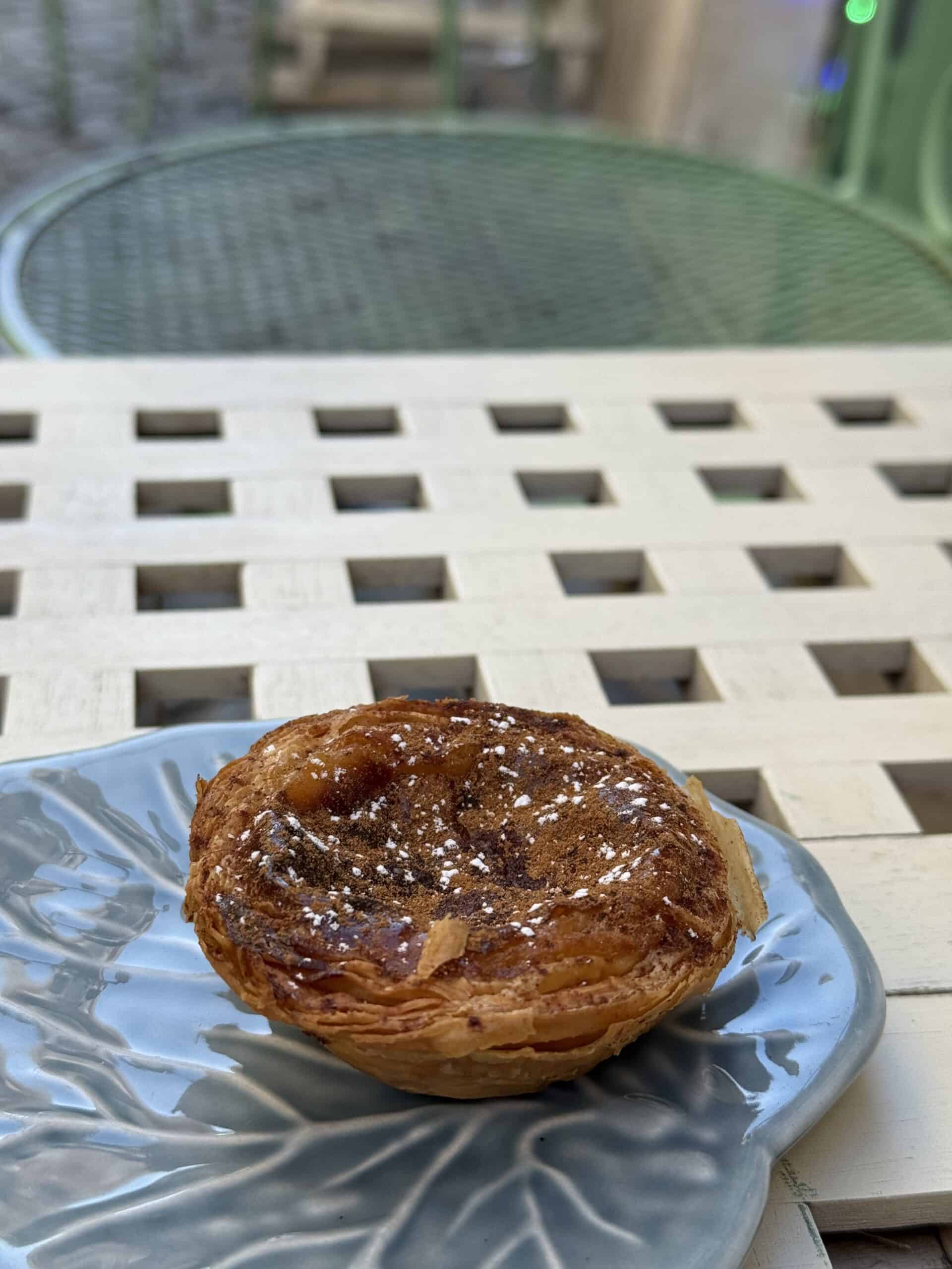 Portuguese pastel de nata topped with cinnamon and powdered sugar on a blue ceramic plate at Casa São Miguel in Alfama, Lisbon.
