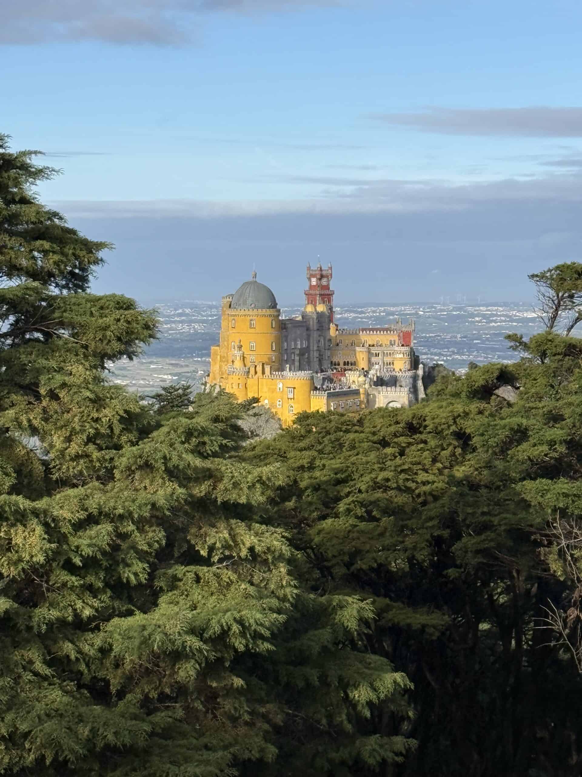 Pena Palace’s yellow walls and red tower rising above the forest in Sintra, Portugal.