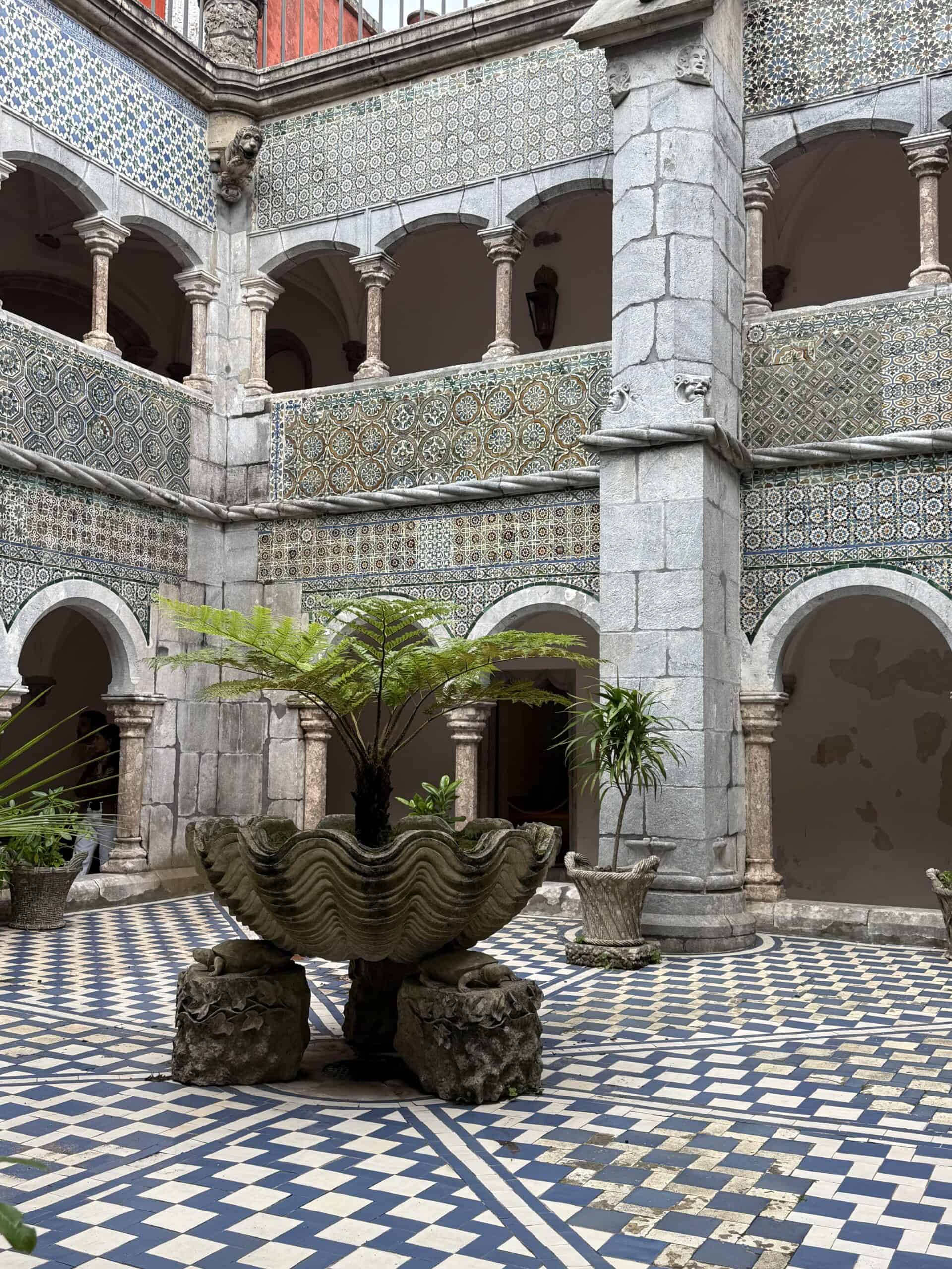 Tiled courtyard inside Pena Palace in Sintra with Moorish-style arches, patterned walls, and a central stone planter.