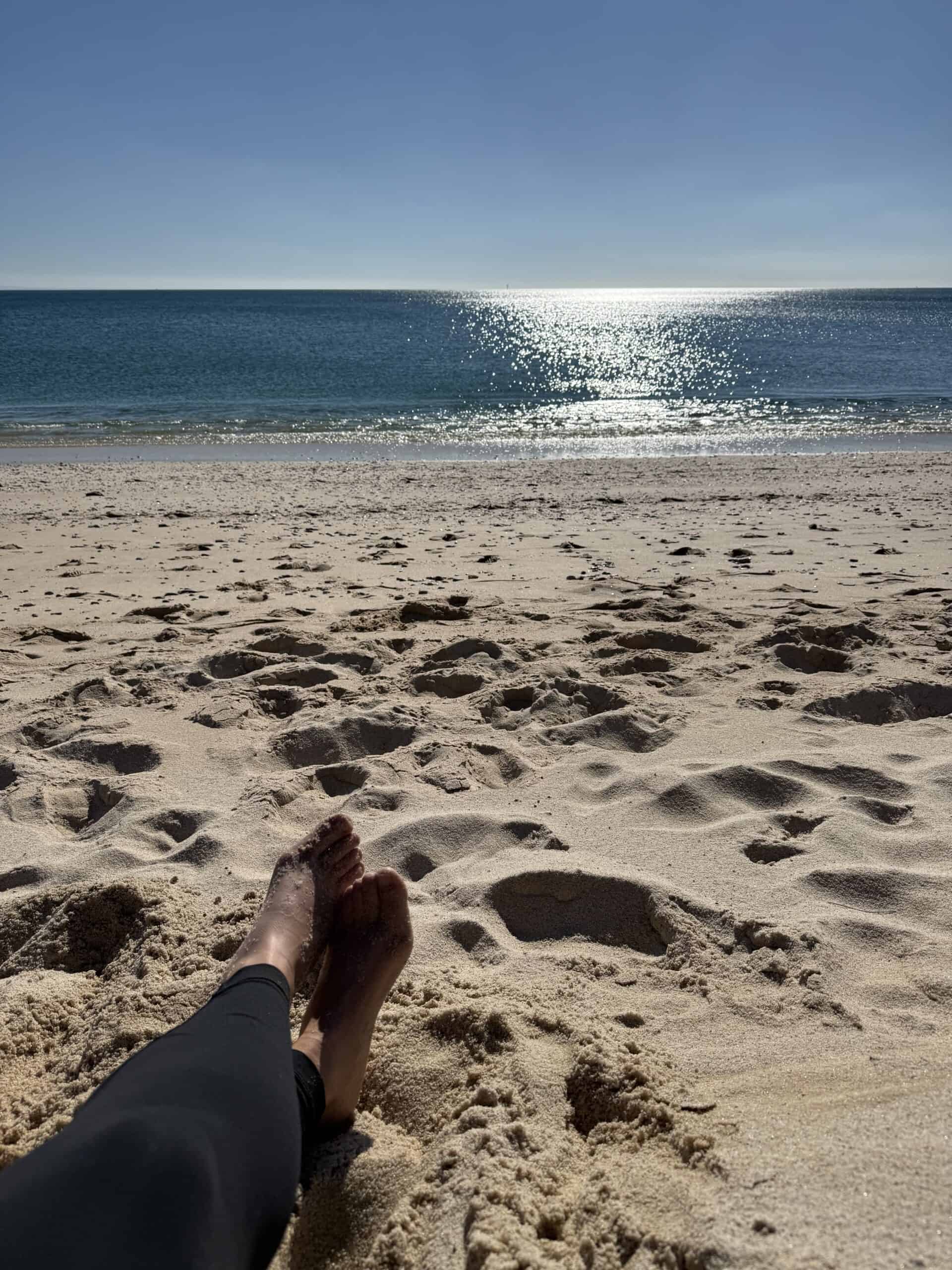Relaxing barefoot on the sandy beach at Praia do Creiro with sunlight reflecting on the sea in Arrábida, Portugal