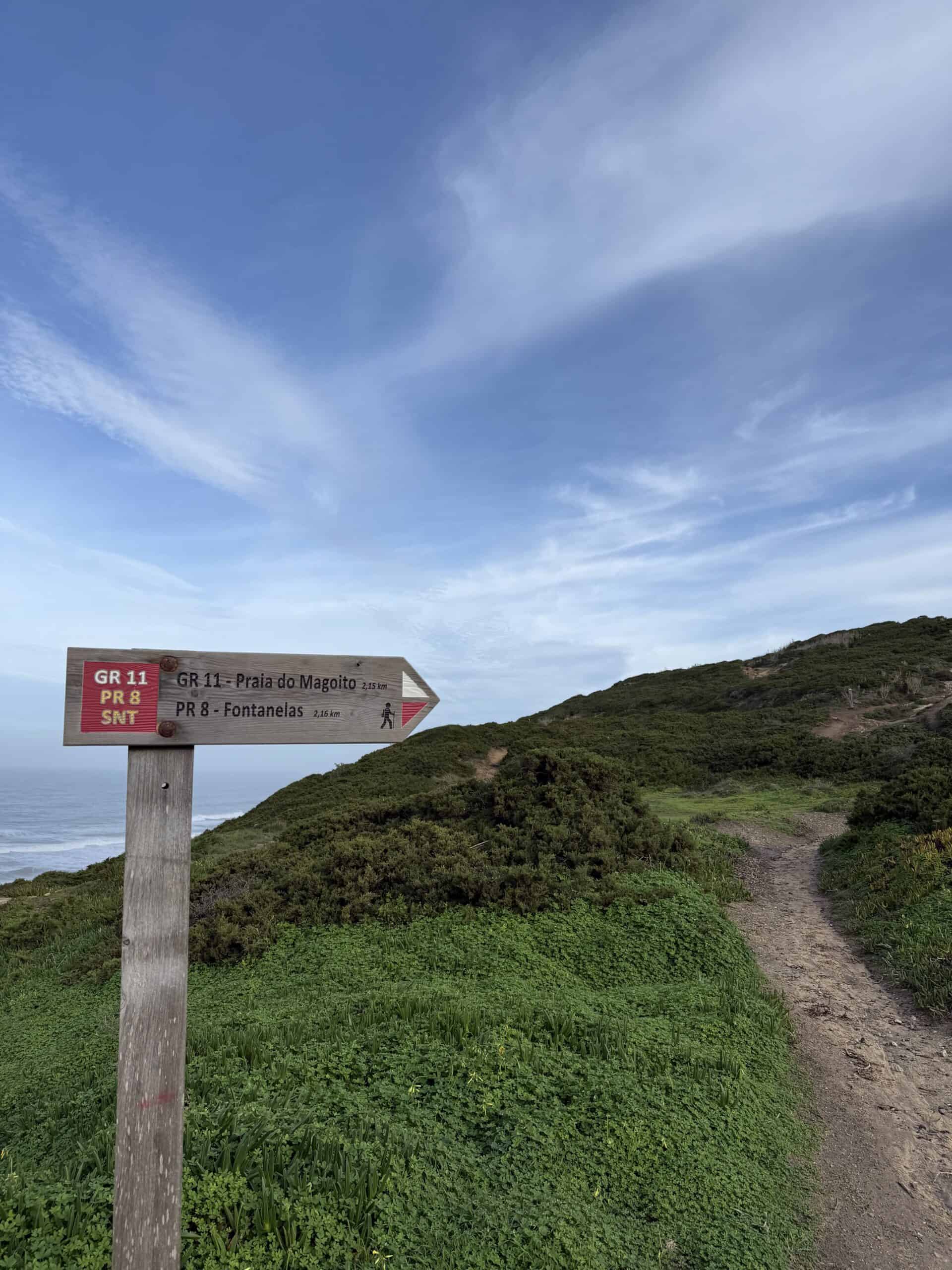Hiking trail sign pointing toward Praia do Magoito along the coast near Sintra, Portugal