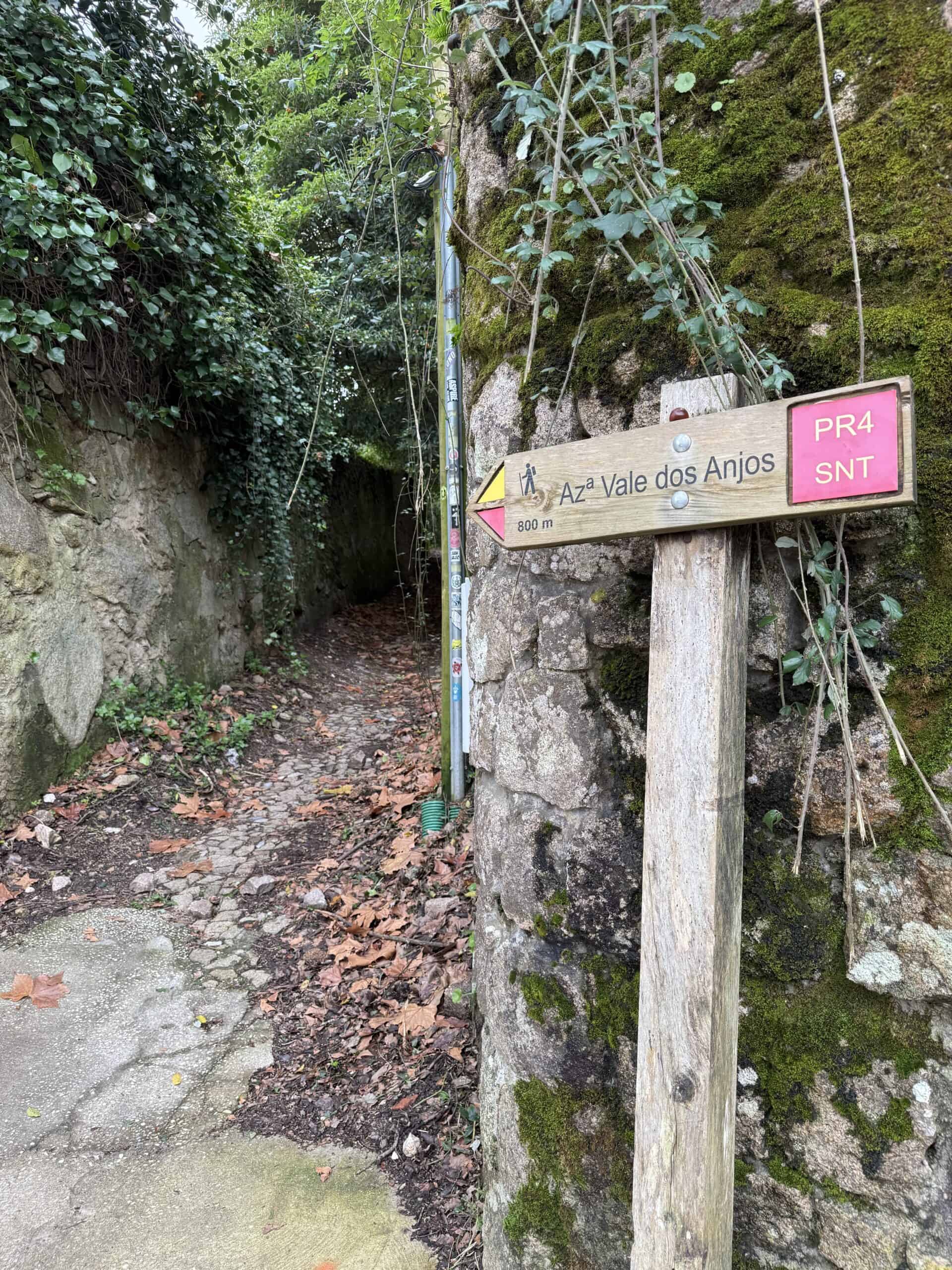 PR4 trail sign pointing toward Vale dos Anjos beside a narrow path between moss-covered stone walls in Sintra.