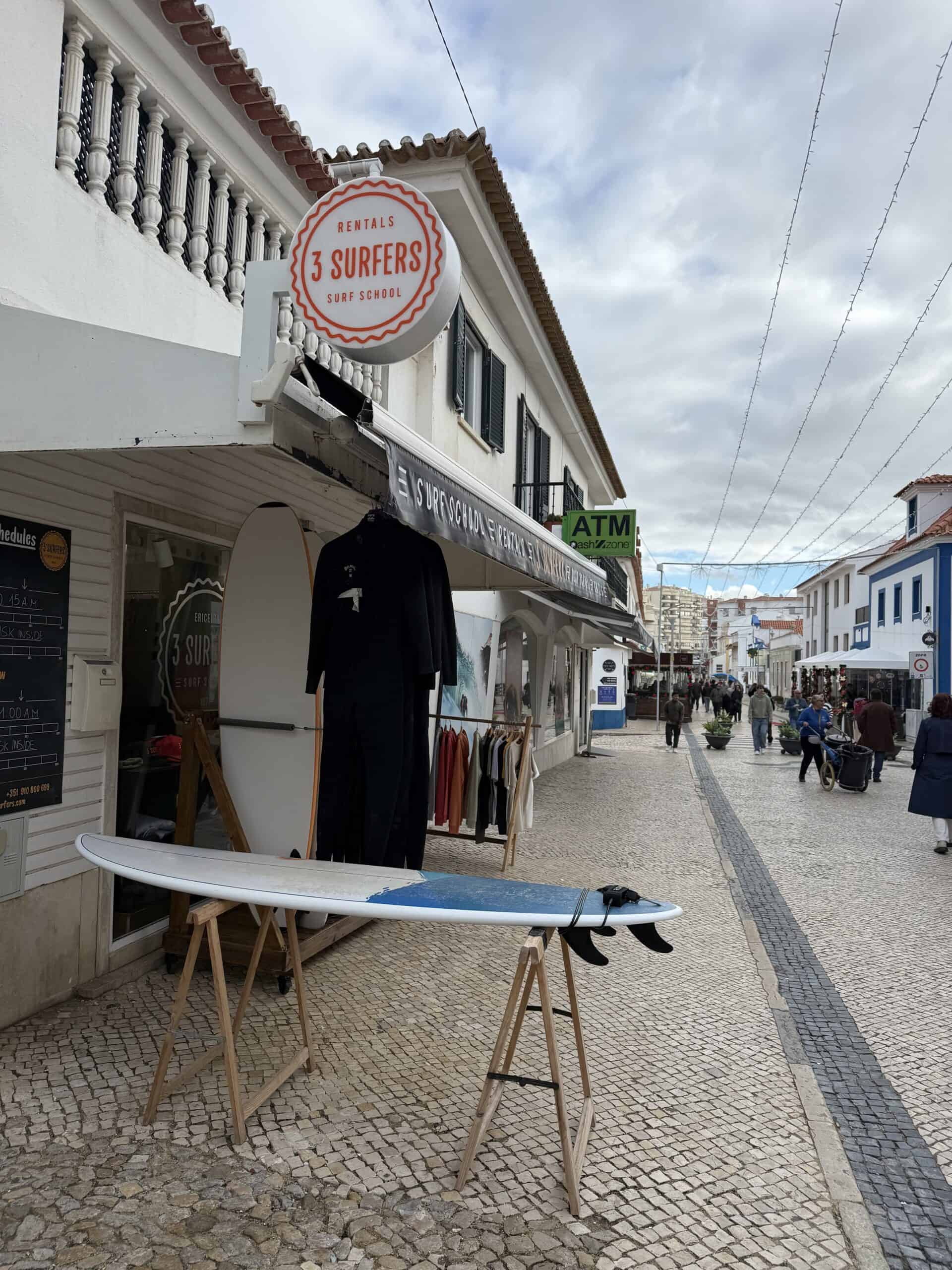 Surf shop with boards and wetsuits along a cobblestone street in Ericeira, Portugal