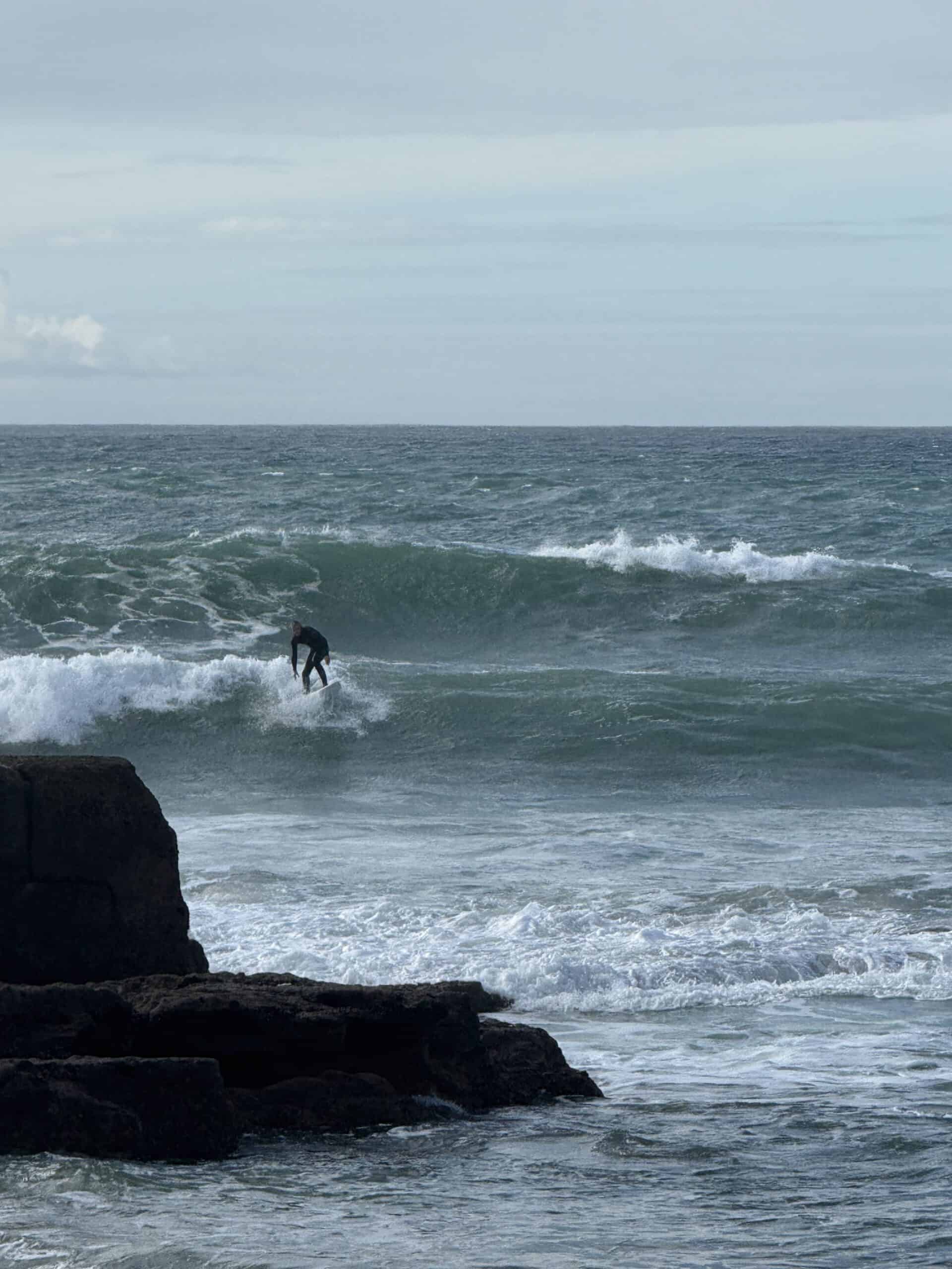 Surfer riding a wave along the rocky coast of Ericeira, Portugal