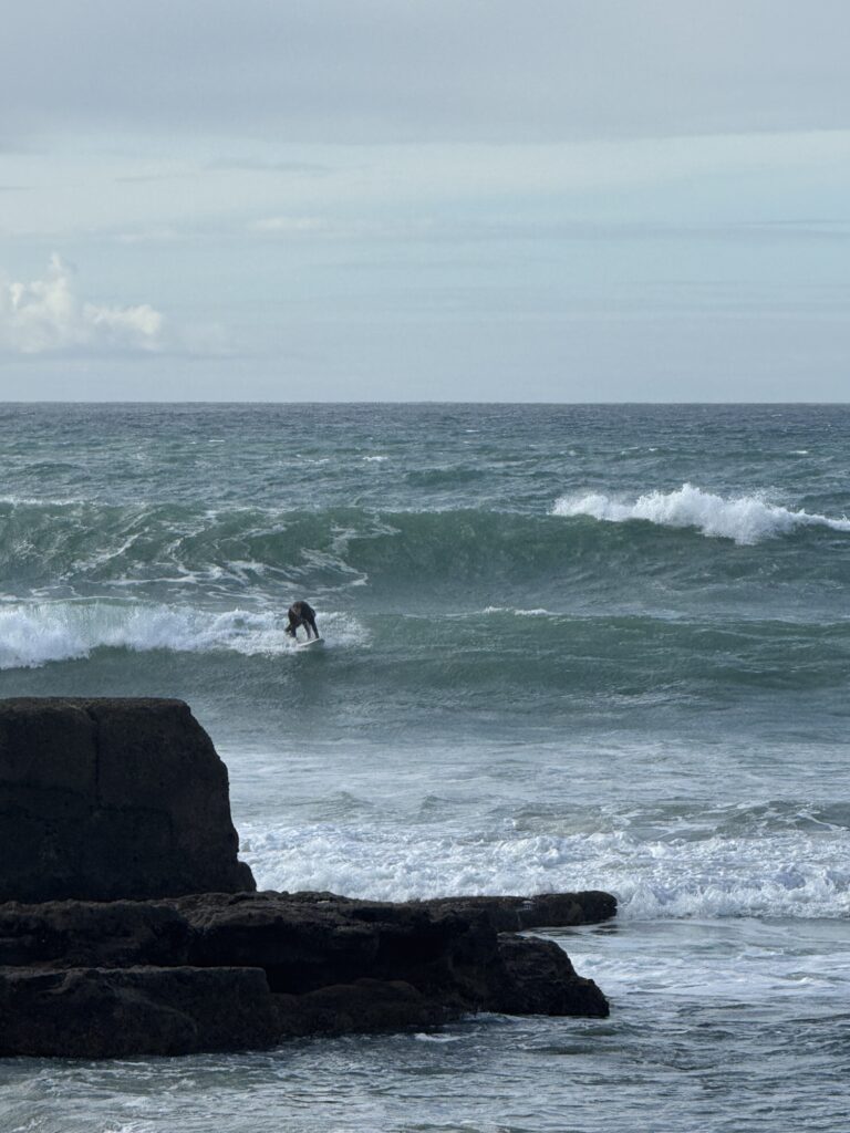 Surfer riding an Atlantic Ocean wave near the rocky coastline of Ericeira, Portugal.