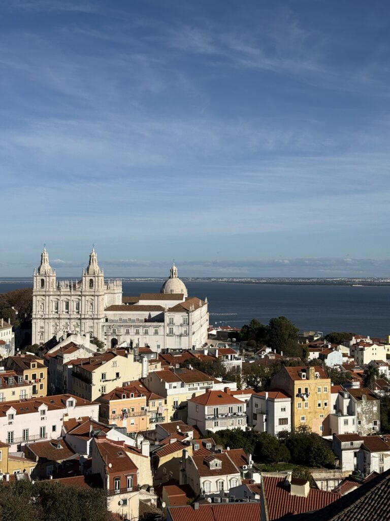 Panoramic view from Torre da Igreja do Castelo de São Jorge overlooking Alfama's terracotta rooftops, the Church of São Vicente de Fora and the Tagus River in Lisbon.