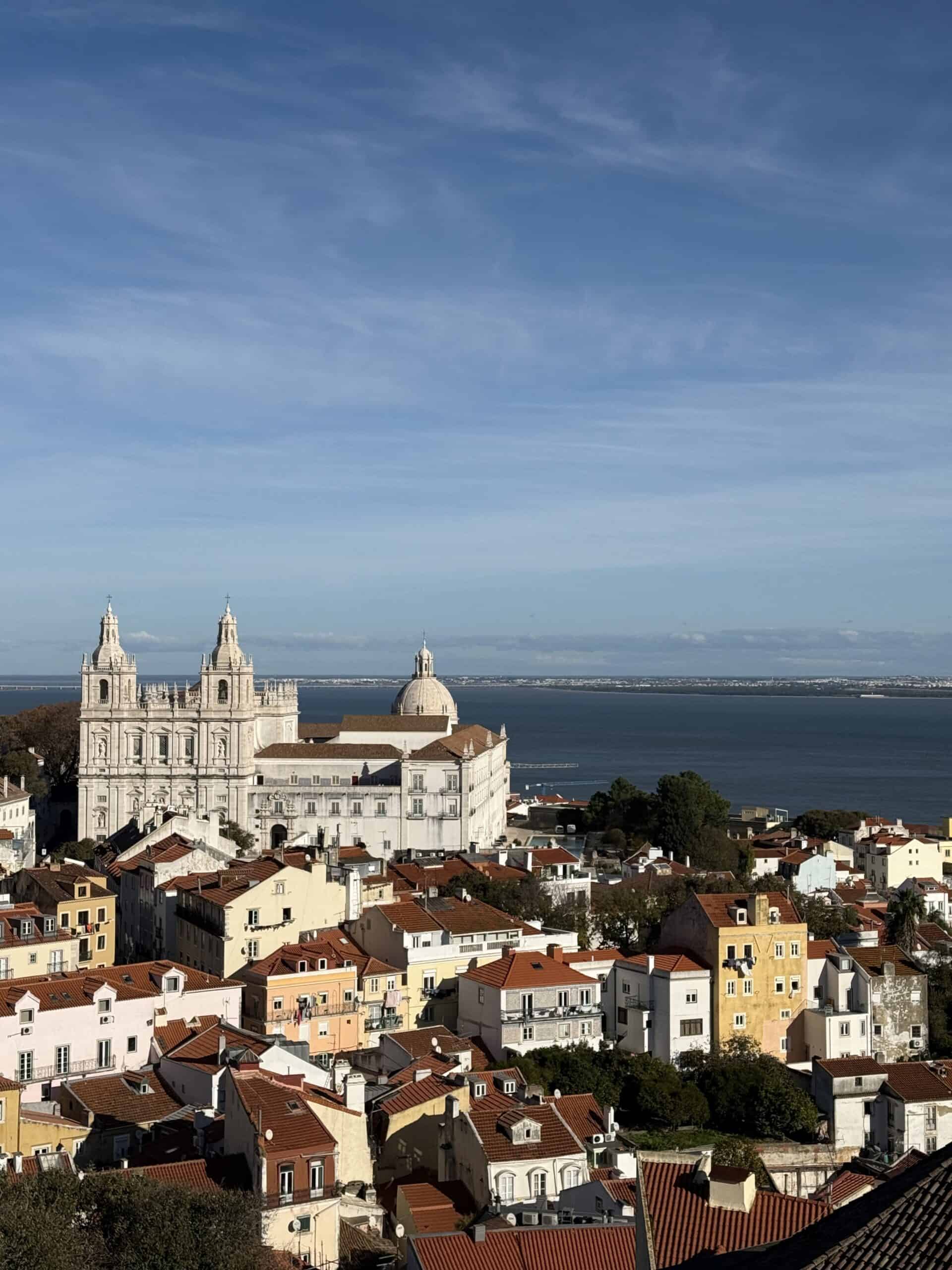 Panoramic view from Torre da Igreja do Castelo de São Jorge overlooking Alfama's terracotta rooftops, the Church of São Vicente de Fora and the Tagus River in Lisbon.