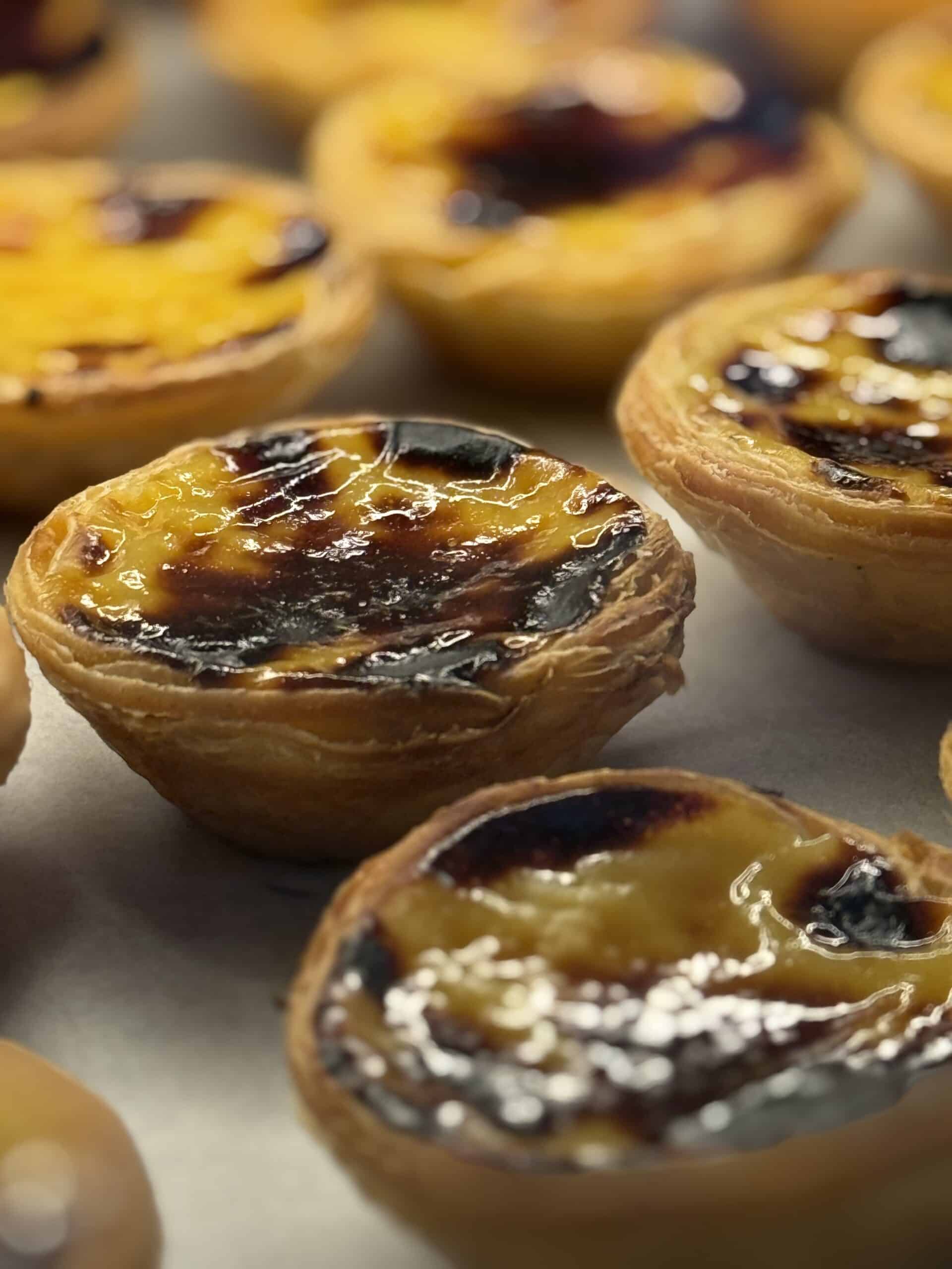 Traditional Portuguese pastéis de nata with golden custard, caramelized tops and flaky pastry crusts.