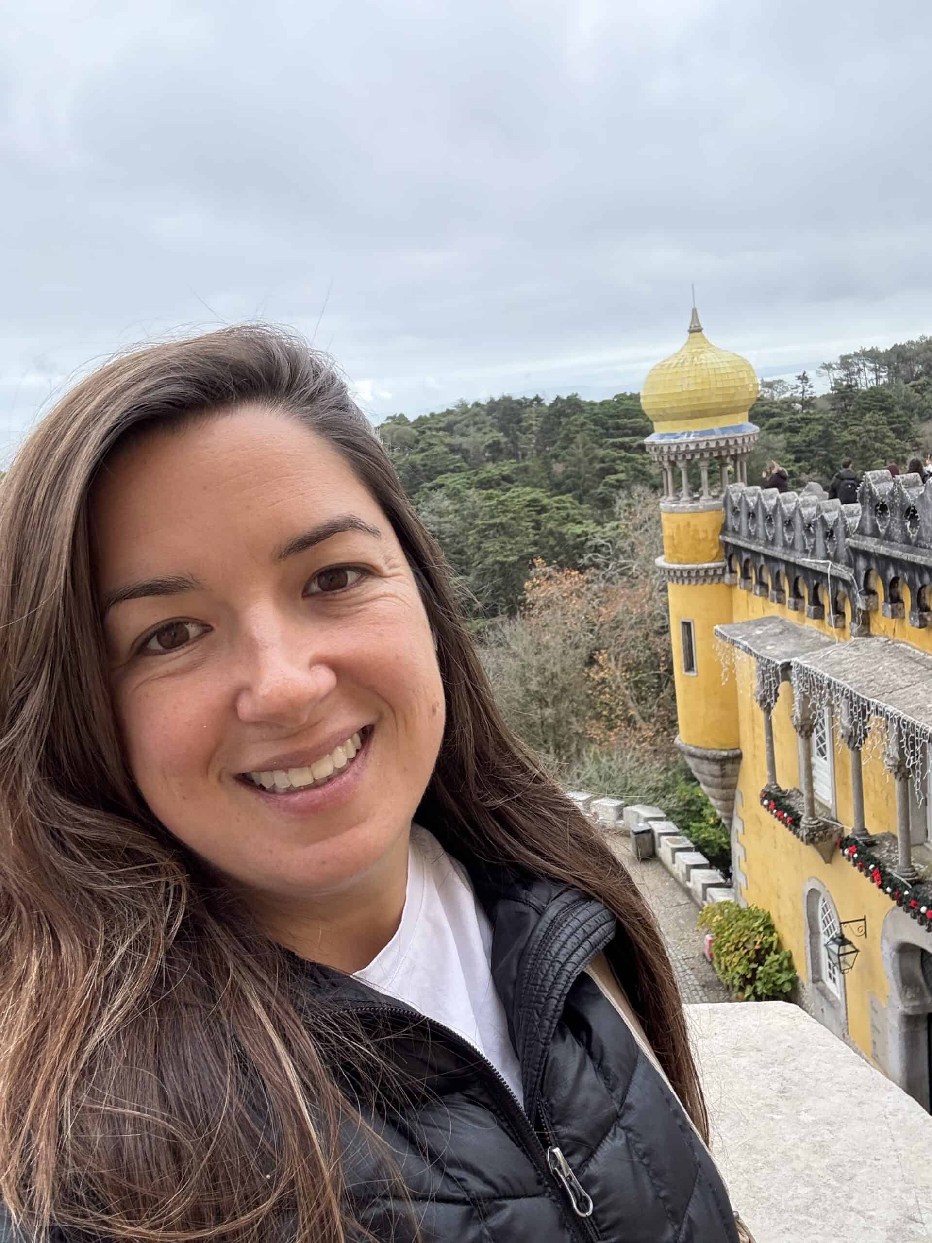 Visitor at Pena Palace in Sintra with the yellow palace tower and forested hills in the background.
